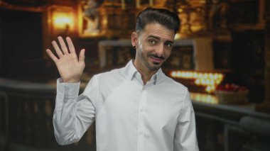 Genç gülümseyen adam el sallıyor mum ışığında kilise koridorunda; dinginlik inancı bağlılık hoşgeldin.