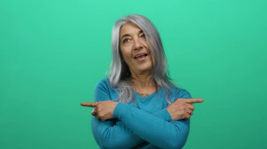 Gri saçlı, mavi kazaklı bir kadın canlı yeşil arka plana karşı yan yan bakıyor. Yön ve pozitifliği neşeli bir ifadeyle aktarıyor..