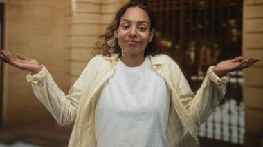 Avuçlarını kaldırıp binanın girişine doğru omuz silken, beyaz tişört ve çizgili tişört giyen, elleri hafifçe havaya kalkmış bir kadın..