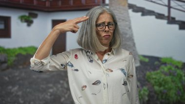 Kadın, somurturken binanın kapısını işaret ediyor, el kaldırıyor; sinir bozucu sınır ayarları.