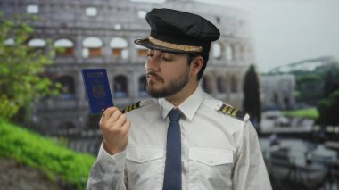 Güneşli bir günde Roma Kolezyumu 'nun dışında elinde pasaport tutan genç pilot üniformalı ve şapkalı seyahat ve turizmi simgeliyor..