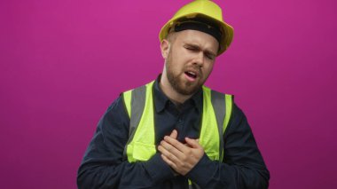 Sarı kasketli ve yelek giyen inşaat işçisi. Stüdyoda elleri mor arkaplan, ekşi; acı..