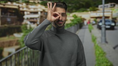 Gri balıkçı yaka kazaklı genç İspanyol adam sokak köşesinde tamam tabelasında el ele tutuşuyor. Onaylandı..