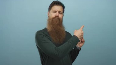 Mavi stüdyo ortamında uzun sakallı, koyu yeşil tişörtlü ve kulağına piercing takan bir adam..