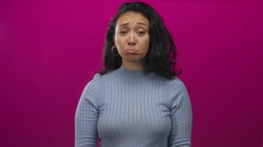Stüdyoda elleri dua jesti ile sıkılmış bir kadın, mor fon ve halka küpe görünür; özür dileme talebi.