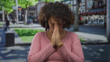 Pembe bluz giyen kadın, güneşli şehir caddesinde duayla el ele tutuşuyor. Bulanık binalar, huzur..