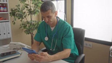 Hastane odasında steteskobu olan üniformalı bir doktor tablete baktığında klinik ortamın kapalı olduğunu gösteriyor..