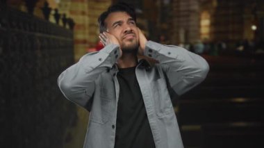 Kilisede elleri kulaklarını tıkayan, kaygısını dile getiren, sıradan giyinmiş İspanyol kökenli, bulanık tarihsel geçmişi olan, düşünceli bir adam..