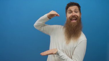 Uzun sakallı adam mavi stüdyoda avuçlarıyla görünmez bir nesne tutuyor; oyunculuk gösterisi.