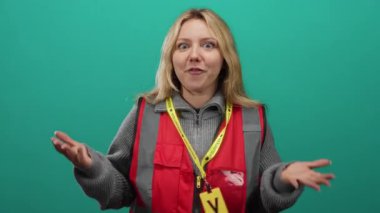 Yeşil arka plana karşı duran, kırmızı yelek giyen gönüllü bir kadın, katılımcılarla el ele tutuşurken rolünün coşkusunu gösteriyor..