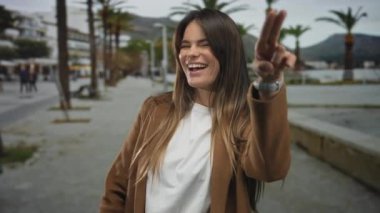 Genç İspanyol kadın neşeli bir şehir caddesinde neşeli hareketler yapıyor, palmiye ağaçları ve şehir binalarıyla çerçevelenmiş, açık hava heyecanı ve canlı enerji yakalıyor..