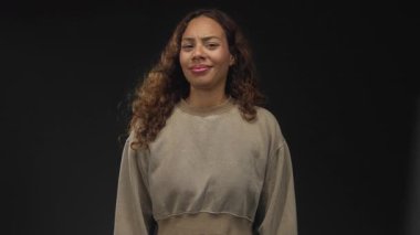 Stüdyoda siyah bir arkaplan ile kırpılmış bir sweatshirt giyerken kadın yüzü eğik, sırıtıyor ve şaşı; sessiz şüphecilik.