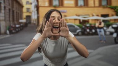 Beyaz tişörtlü kadın, elleri ağıza dayayıp yaya geçidinde bağırıyor. Gençlik heyecanı..