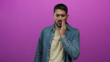 Pembe arka planda diş ağrısı çeken bir adam yanağına dokunurken rahatsız ve sıkıntılı görünüyor..