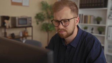 Ofisteki bilgisayar ekranına kaşlarını çatmış, çatık kaşlı, gözlüklü ve sakallı bir adam monitörü kontrol ederken öne eğiliyor, ofis raflarını görünür hale getiriyor; hayal kırıklığı.