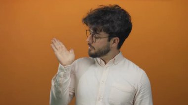 Genç İspanyol sakallı, elleri dışa doğru uzanan canlı turuncu arka plan gözlüklü ve beyaz gömlekli üç karede kafa karışıklığı ya da belirsizlik gösteren genç bir adam..