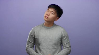 Gri kazaklı genç adam mor arka planda, sakin bir ifadeyle, gözleri kapalı ve hafif bir gülümsemeyle, huzurlu ve rahat bir ruh hali içinde duruyor..