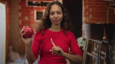 Elma tutan kadın ve parmaklar binanın içini işaret ediyor, el meyveyi kavrarken ileriye dönük hareketi işaret ediyor; sağlıklı seçim özgüveni.