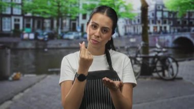 Önlüklü kadın, kanal ve bina kenarlarında parmaklarını çimdikliyor, ellerini ve hareketlerini gösteriyor; güven öğretimi.