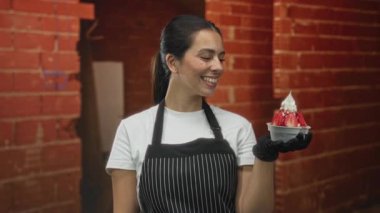 İnce çizgili önlük giymiş bir kadın, eldiven takmış bir el üzerinde çilek tatlısı tutuyordu. Tuğla duvarlı bina içinde, fincana gülümsüyordu. Neşeli bir servis..