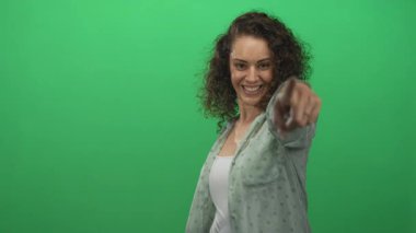 Genç İspanyol kadın, yeşil stüdyoda parmaklarını göstererek kalp şekli veriyor..