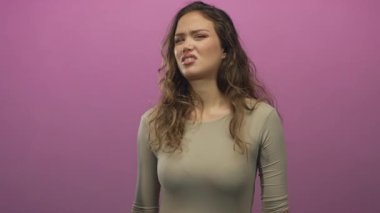 Pembe arka planda iğrendiğini ifade eden bir kadın, stüdyo ortamında güçlü bir duygusal tepkiyi gösteriyor ve genç İspanyol bir kadın onaylamıyor..