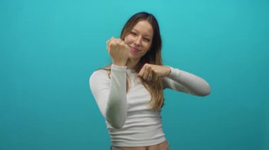 Turkuaz stüdyoda orta parmak ve sıkılmış yumruklar gösteren bir kadın. Uzun kollu ve kot pantolonlu bir kadın..