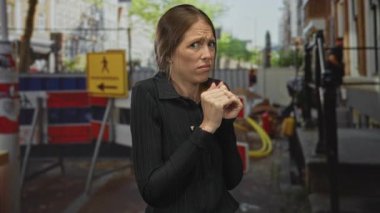 Barikatın yanında el kaldıran genç İspanyol kadın ve inşaat alanında uyarı işareti; kaçınma tiksintisi.