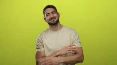 Genç adam güven içinde kollarını kavuşturup neşeli sarı arka plana karşı gülerek arkadaşlığı ve pozitifliği tasvir ediyor.