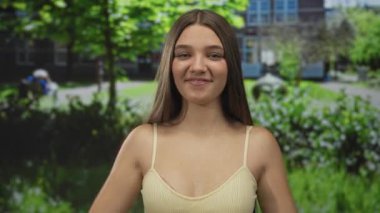 Genç kız, binanın önündeki yeşil parktaki sarı kollu tişörtle sıkılmış yumruklarını ve çıplak kollarını kaldırıyor..