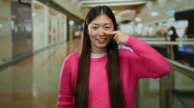 Modern alışveriş merkezinin içinde renkli süveter giyen bir kadın alışveriş merkezinde neşeli bir ifade sergiliyor ve canlı bir iç mekan atmosferi yakalıyor..