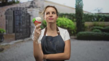 Eldivenli ve kolları bina girişinde çaprazlanmış dondurma külahını tutan kadın; yaz keyfi.