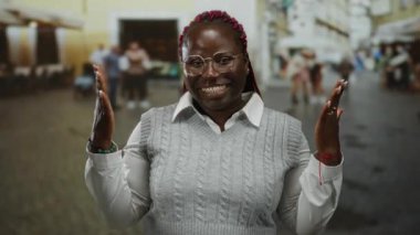 Dışarıda gülümseyen bir kadın, şehirde elleri gözlüklü ve örgülü bir süveterle dürbünlü jest yapıyor..