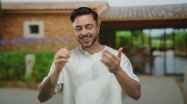 Sakallı genç adam, yazın güneşli bir günde şehir binalarıyla çevrili günlük gömleğiyle şehir sokaklarında gülüyor..