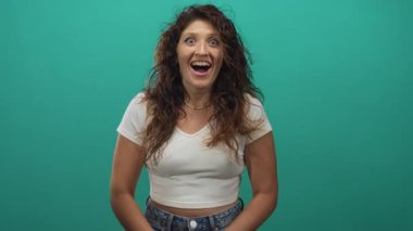 Elleri yanaklarında gülümseyen, çilli yüzünü gösteren, beyaz bluz ve kot pantolon giyen, neşeli bir kadın..