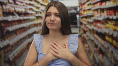 Kafkas ergen kız süpermarkette market rafları arasında iki eliyle göğsünü sıkıca kavrıyor; gerginlik gerilimi.