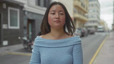 Şehir sokaklarında genç bir kadın mavi kazak giyiyor ve şehir planına karşı ciddi bir ifade sergiliyor.