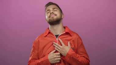 Turuncu tulumlu genç adam yüzü kapalı pembe bir stüdyoda hafif bir gülümseme, sakin bir kabullenme..