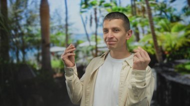 İki eli de yemyeşil park geçmişine güvenle gülümseyen adam para hareketi yapıyor.