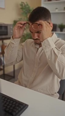 Adam uzun bir çalışma seansından sonra gözlüğünü çıkarır ve ofis binasında baş ağrısı için alnını tutar; yorgunluk.