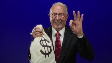 Takım elbiseli kıdemli bir adam elinde para çantası ve üzerinde dolar işareti olan mavi arka planda zenginlik ve yolsuzluğu gösteren bir işaret var..