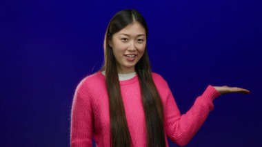 Mavi arka planda poz veren, pembe süveter giyen, gülümseyen ve anlamlı, canlı bir karakteri tek başına yakalayan bir kadın..