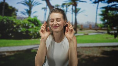 Palmiye ağaçlarının yakınındaki yeşil bir parkta gülümseyen beyaz bir kadın ve alçak duvarın yanında asfalt bir yol; umut dolu..