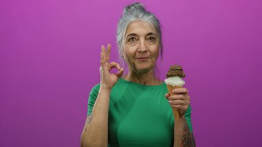 Kıdemli kadın çikolatalı dondurma külahının keyfini çıkarıyor, canlı pembe bir duvara yaslanıyor, yeşil giyiniyor, keyif ve onayını veriyor..