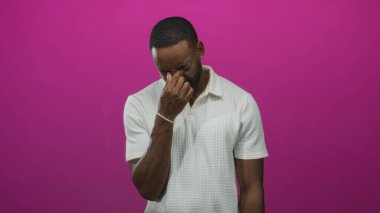 Pembe arka plan, beyaz polo tişört ve mide bulantısına karşı burnunu stüdyoya sokan bir adam..