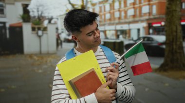 Elinde İtalyan bayrağı ve klasörleri olan genç bir adam şehir merkezinde kültürel gurur ve eğitim duygusunu iletiyor..