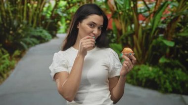 Orman yolunda sessiz kalmak için parmak dudağa kek tutan genç İspanyol kadın; günaha teşvik diyet kontrolü.