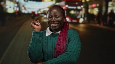 Gece kalabalık bir caddede saçları örgülü, açık havada gülümseyen bir kadın canlı ışıklar ve hareketli bir arka planla çerçevelenmiş..