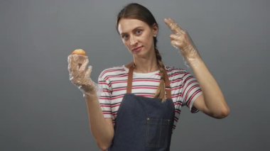 Kotlu önlüklü kadın gri stüdyoda elleri ve parmakları eldivenli muffin tutuyor. Mutfak hüsranı..