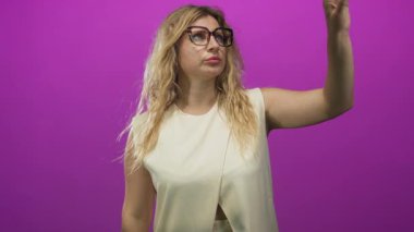 Büyük boy gözlüklü ve bej kolsuz bluzlu bir kadının işaret parmağı morumsu stüdyoda yukarı doğru..